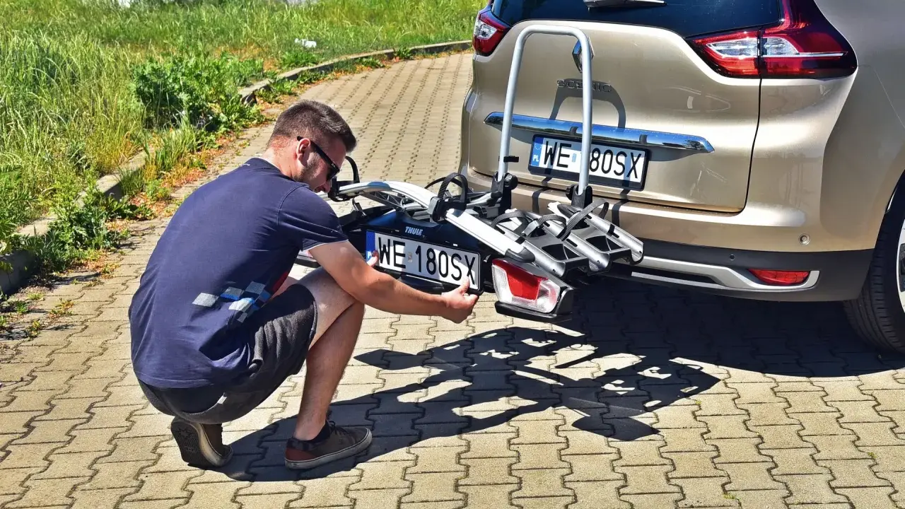Mężczyzna montuje tablicę rejestracyjną na bagażnik rowerowy zamontowany z tyłu samochodu.