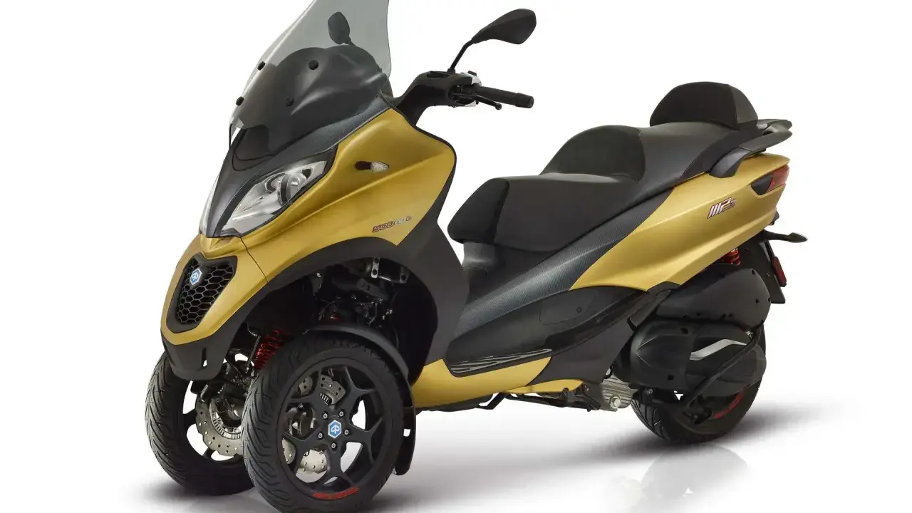 Złoty Piaggio MP3 500, trójkołowy skuter, gotowy do osiągnięcia swojej maksymalnej prędkości.