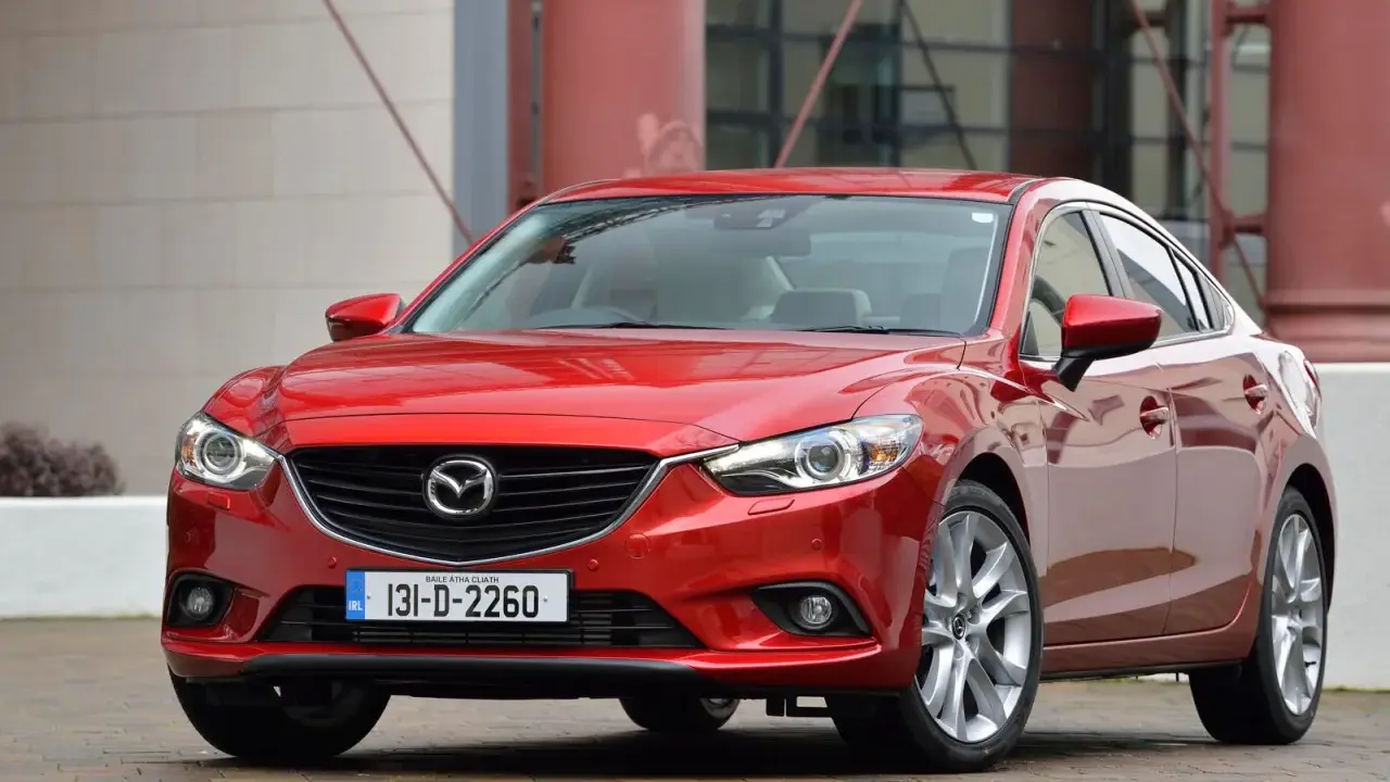 Czerwona Mazda 6, reprezentantka klasy D samochodów, prezentuje się elegancko na tle nowoczesnej architektury.
