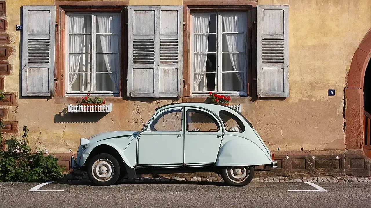 Jasnoniebieski, zabytkowy Citroen 2CV, jeden z tych klasycznych, francuskich modele stare, stoi przed kamiennym domem z drewnianymi okiennicami.