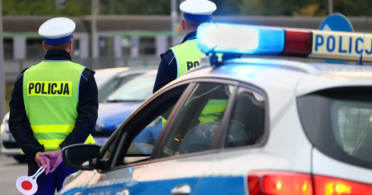 Policjanci w kamizelkach odblaskowych stoją przy radiowozie. Zastanawiasz się, ile można jechać poza terenem zabudowanym?