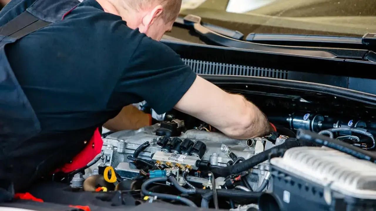 Mechanik pracuje przy silniku z instalacją gazową. Sprawdza podzespoły, by zapewnić optymalną cng cenę za litr.
