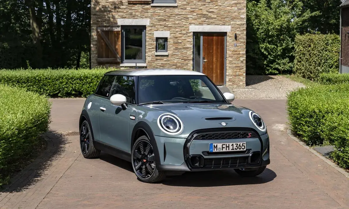 Nowoczesny Mini Cooper w kolorze miętowym stoi przed kamiennym domem. Zastanawiasz się, ile pali ten model?