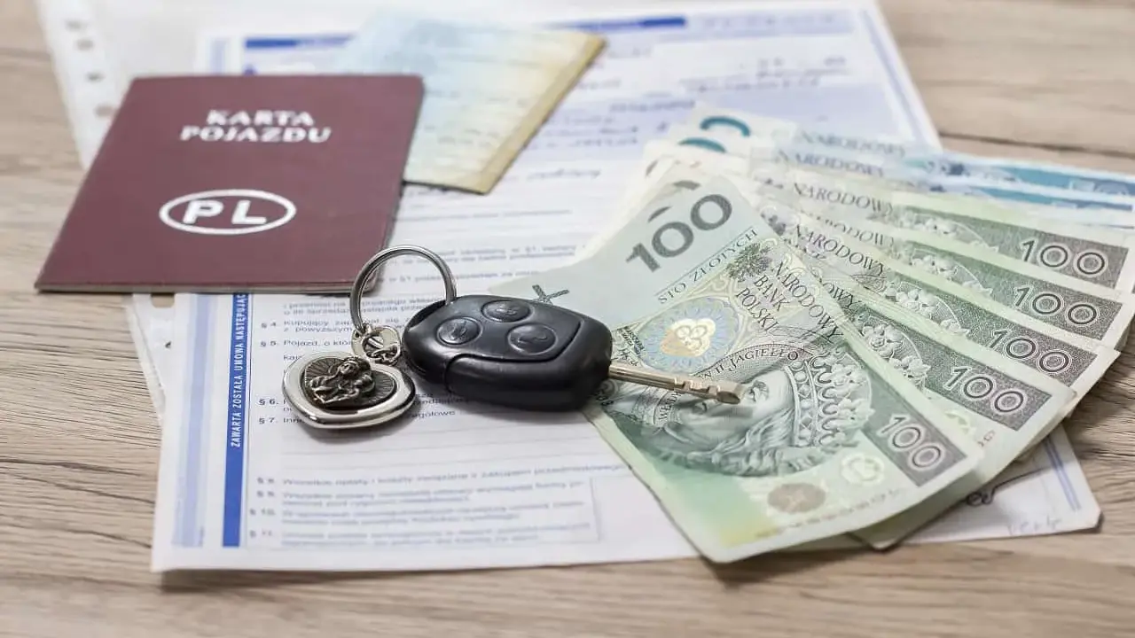 Karta pojazdu, kluczyki i polskie banknoty 100 zł leżą na dokumentach.