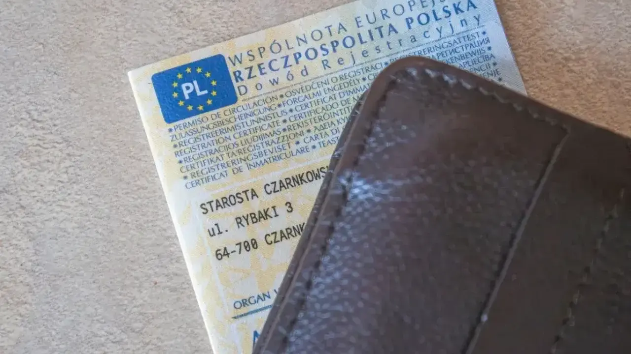 Dowód rejestracyjny pojazdu i brązowy portfel. Nieodebranie dokumentu może skutkować karą za nieodebranie dowodu rejestracyjnego.