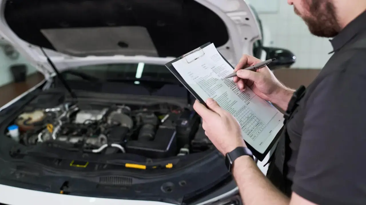 Mechanik sprawdza listę kontrolną przed przeglądem samochodu, zastanawiając się, ile kosztuje przegląd.