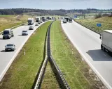 Ciężarówki na autostradzie pędzą z dużą prędkością, pokonując kolejne kilometry. W tle widać inne pojazdy i krajobraz.
