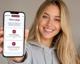Uśmiechnięta kobieta trzyma telefon z aplikacją PWPW. Na ekranie widać opcję "Rezerwacja egzaminu" i "Zapis na egzamin WORD online".