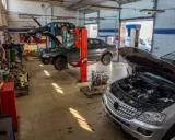 Warsztat samochodowy z kilkoma autami na podnośnikach. Widać m.in. ciemny sedan, który wygląda jak p1351 peugeot, oraz srebrny SUV z otwartą maską.