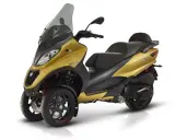 Złoty Piaggio MP3 500, trójkołowy skuter, gotowy do osiągnięcia swojej maksymalnej prędkości.
