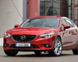 Czerwona Mazda 6, reprezentantka klasy D samochodów, prezentuje się elegancko na tle nowoczesnej architektury.