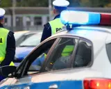 Policjanci w kamizelkach odblaskowych stoją przy radiowozie. Zastanawiasz się, ile można jechać poza terenem zabudowanym?