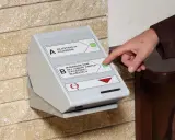Dłoń naciska przycisk na automacie do wydawania dowodów rejestracyjnych, ułatwiając wymianę dowodu rejestracyjnego online.