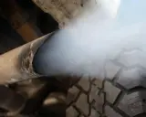 Dym z rury wydechowej, wskazujący na przedmuchy w silniku diesla. Widać fragment opony i podwozia pojazdu.