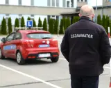 Egzaminator w czarnej kurtce z napisem "EGZAMINATOR" obserwuje czerwony samochód z literą "L" na dachu. Jak odwołać egzamin na prawo jazdy infocar?