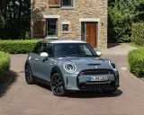 Nowoczesny Mini Cooper w kolorze miętowym stoi przed kamiennym domem. Zastanawiasz się, ile pali ten model?
