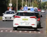 Samochody z literą "L" na dachu i tabliczką "EGZAMIN" czekają na egzamin na prawo jazdy.