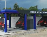 Nowoczesna myjnia bezdotykowa z niebieskimi elementami i reklamami czerwonych samochodów.