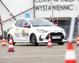Biały samochód szkoleniowy z literą "L" na dachu i pachołkami na placu manewrowym. To miejsce, gdzie nauczysz się, jak wypełnić pkk.