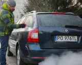 Mężczyzna w zimowej kurtce czyści zamarzniętą szybę auta. Dym z rury wydechowej sugeruje, że to diesel i właśnie próbuje się dowiedzieć, jak odpalić diesla w mroźny dzień.