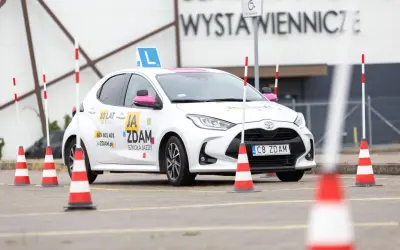 Biały samochód szkoleniowy z literą "L" na dachu i pachołkami na placu manewrowym. To miejsce, gdzie nauczysz się, jak wypełnić pkk.