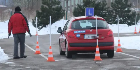 Czerwony samochód z literą "L" na dachu i naklejką "EGZAMIN" na tylnej klapie, otoczony pachołkami na placu manewrowym. To miejsce, gdzie bije rekord zdawania prawa jazdy.