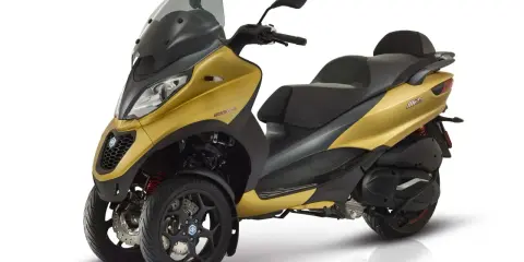 Złoty Piaggio MP3 500, trójkołowy skuter, gotowy do osiągnięcia swojej maksymalnej prędkości.