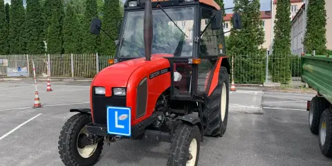 Czerwony traktor Zetor z tabliczką "L" na masce, gotowy do egzaminu na prawo jazdy na traktor.