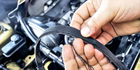 Uszkodzony pasek osprzętu, który wymaga wymiany, widać na dłoniach mechanika.