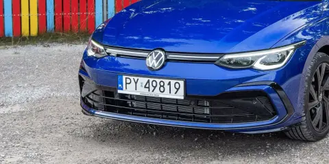 Niebieski Volkswagen Golf R z tablicą rejestracyjną PY 49819, zaparkowany przy kolorowym płocie.