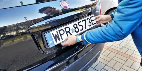 Mężczyzna montuje tablicę rejestracyjną. Pamiętaj o ważności dowodu rejestracyjnego, aby uniknąć problemów.