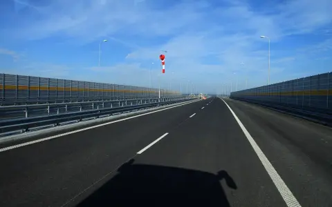 Pusta jezdnia nowej drogi z barierami dźwiękochłonnymi i wiatrowskazem.