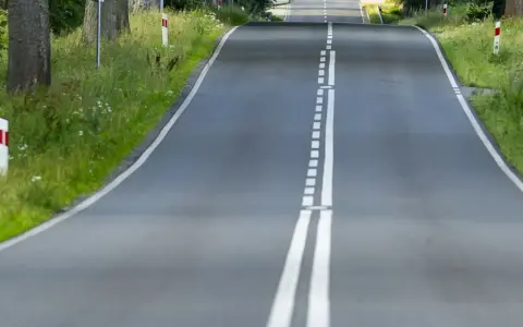 Droga wijąca się wśród zieleni, z podwójną białą **linią ciągłą** pośrodku.