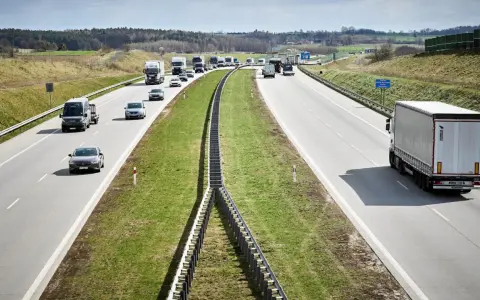 Ciężarówki na autostradzie pędzą z dużą prędkością, pokonując kolejne kilometry. W tle widać inne pojazdy i krajobraz.