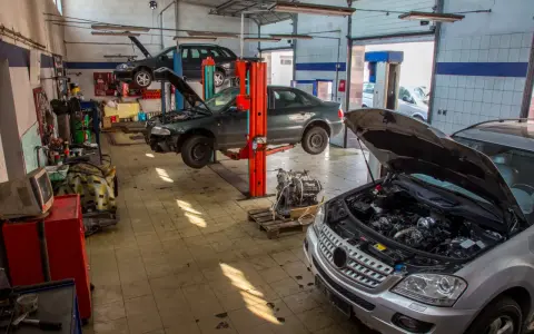 Warsztat samochodowy z kilkoma autami na podnośnikach. Widać m.in. ciemny sedan, który wygląda jak p1351 peugeot, oraz srebrny SUV z otwartą maską.