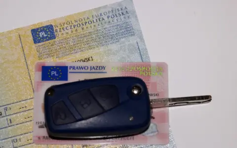 Kluczyk samochodowy leży na dowodzie rejestracyjnym i prawie jazdy. To komplet dokumentów do prowadzenia pojazdu.