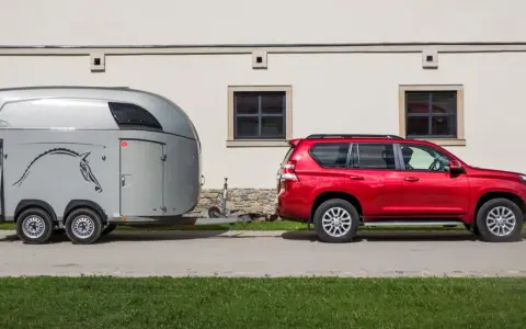 Czerwony SUV holuje przyczepę kempingową z koniem. Jaka kategoria na auto? SUV z przyczepą do przewozu zwierząt.