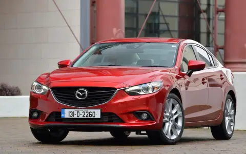 Czerwona Mazda 6, reprezentantka klasy D samochodów, prezentuje się elegancko na tle nowoczesnej architektury.
