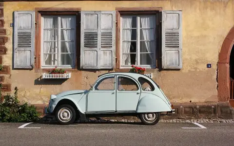 Jasnoniebieski, zabytkowy Citroen 2CV, jeden z tych klasycznych, francuskich modele stare, stoi przed kamiennym domem z drewnianymi okiennicami.