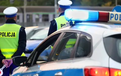 Policjanci w kamizelkach odblaskowych stoją przy radiowozie. Zastanawiasz się, ile można jechać poza terenem zabudowanym?
