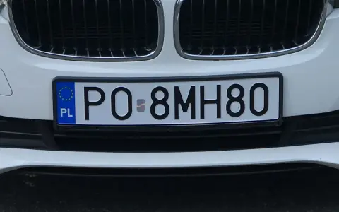 Biała tablica rejestracyjna z kodem PO 8MH80, z niebieskim paskiem UE i literami PL.