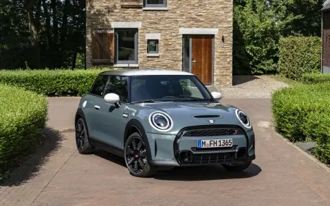 Nowoczesny Mini Cooper w kolorze miętowym stoi przed kamiennym domem. Zastanawiasz się, ile pali ten model?
