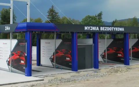 Nowoczesna myjnia bezdotykowa z niebieskimi elementami i reklamami czerwonych samochodów.