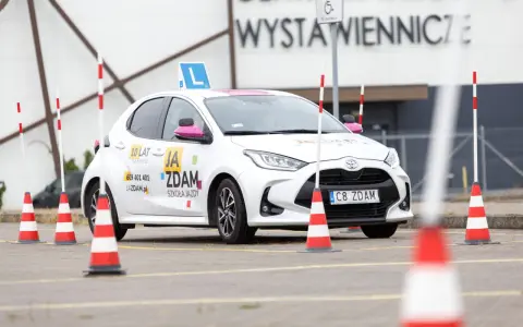 Biały samochód szkoleniowy z literą "L" na dachu i pachołkami na placu manewrowym. To miejsce, gdzie nauczysz się, jak wypełnić pkk.