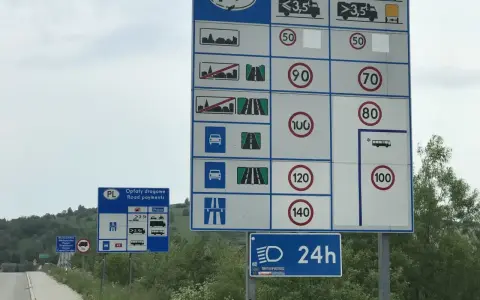 Znaki drogowe informujące o opłatach i limitach prędkości na drodze dwujezdniowej dwukierunkowej.