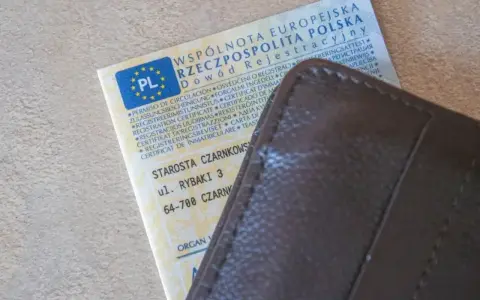 Dowód rejestracyjny pojazdu i brązowy portfel. Nieodebranie dokumentu może skutkować karą za nieodebranie dowodu rejestracyjnego.