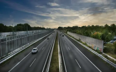 Szeroka autostrada z samochodami, wjazd na autostradę w tle, po bokach ekrany akustyczne i drzewa.