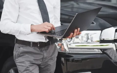 Mężczyzna w koszuli i krawacie sprawdza na laptopie, kiedy trzeba przerejestrować auto.