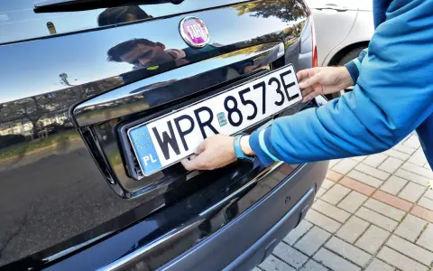 Mężczyzna montuje tablicę rejestracyjną. Pamiętaj o ważności dowodu rejestracyjnego, aby uniknąć problemów.