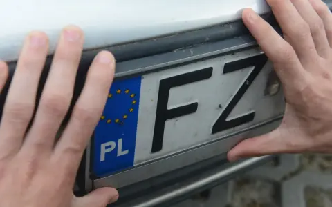 Dłonie trzymają tablicę rejestracyjną z oznaczeniem FZ.